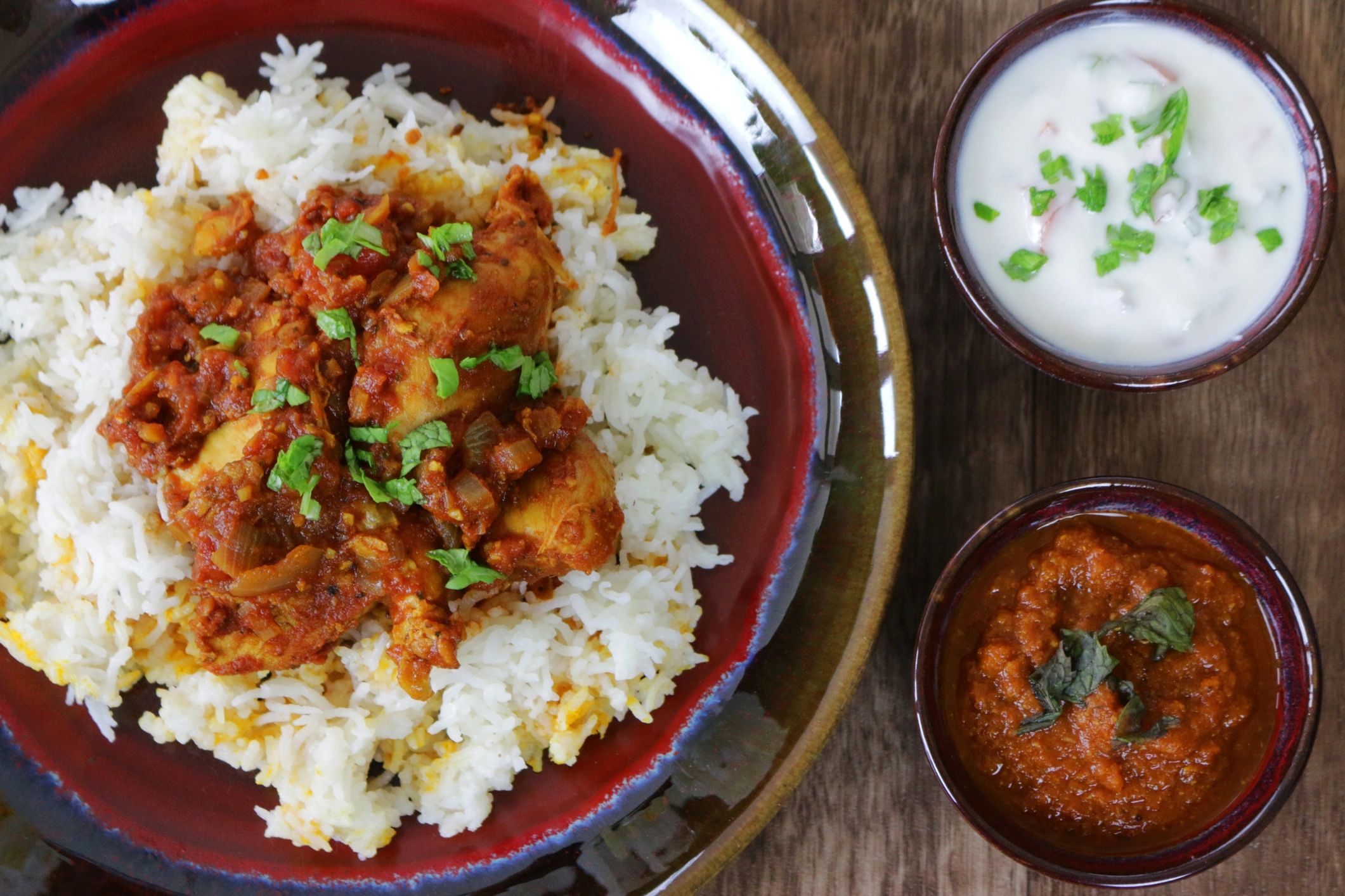Chicken biryani with sauces and raita on a wooden table